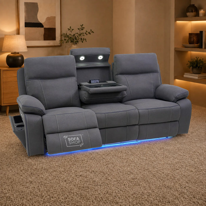 A gray reclining loveseat sofa with built-in headrest screens, a center console tray table, and blue LED underglow, shown in a staged living room setting on a beige carpet.